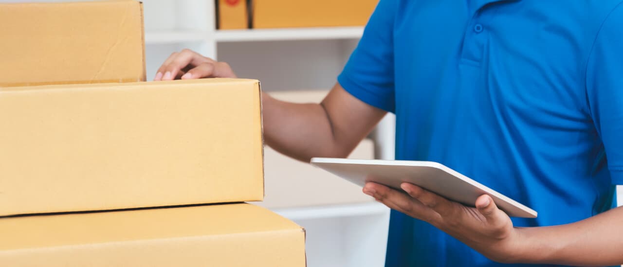 Coordinador logístico revisando una tableta junto a cajas listas para despacho (imagen de referencia)